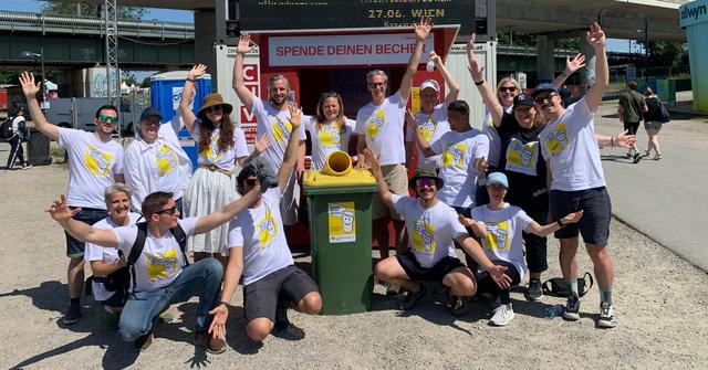 Eine Gruppe Menschen steht am Festivalgelände vor einem Holzstand für die Rückgabe von Bechern.