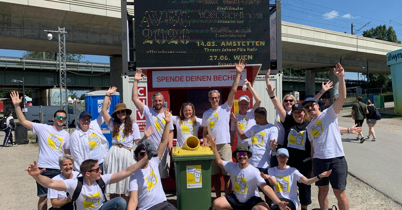 Eine Gruppe Menschen steht am Festivalgelände vor einem Holzstand für die Rückgabe von Bechern.