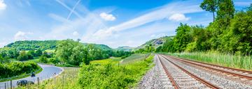 Schienengleise und Straße zwischen grüner Landschaft
