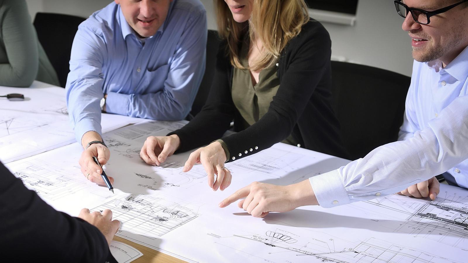 Drei Mitarbeiter:innen sitzen an einer Skizze und zeigen darauf.