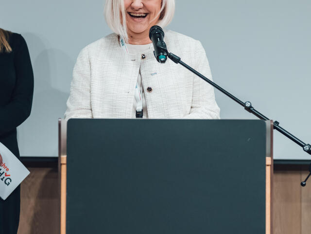 Ivanka Terzic steht an einem Sprecherpult und lächelt.