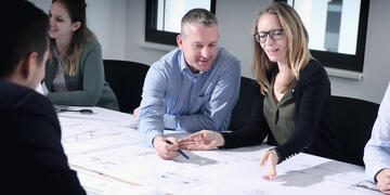 Mitarbeitende sitzen an einem Besprechungstisch und zeigen auf eine Karte.