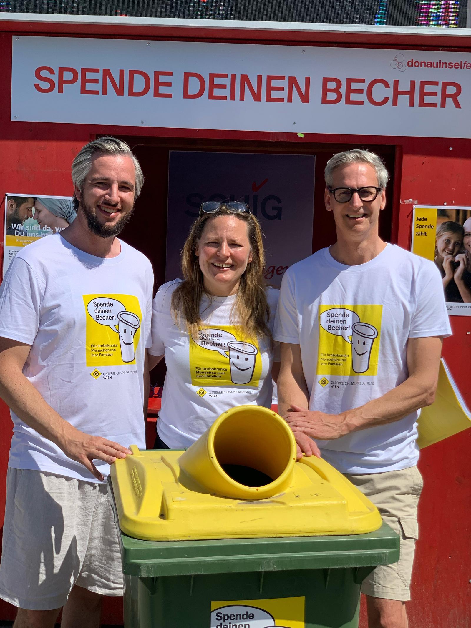 Die zwei SCHIG Geschäftsführer und die Krebshilfe Wien Geschäftsführerin stehen hinter einer Mülltonne zum Entsorgen von Festivalbechern.