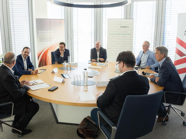 Mehrere Personen sitzen an einem runden Tisch zu einem Gespräch.