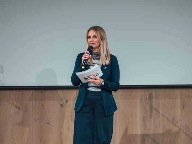Tamara Riedl-Joven moderiert mit einem Mikrophon in der Hand.