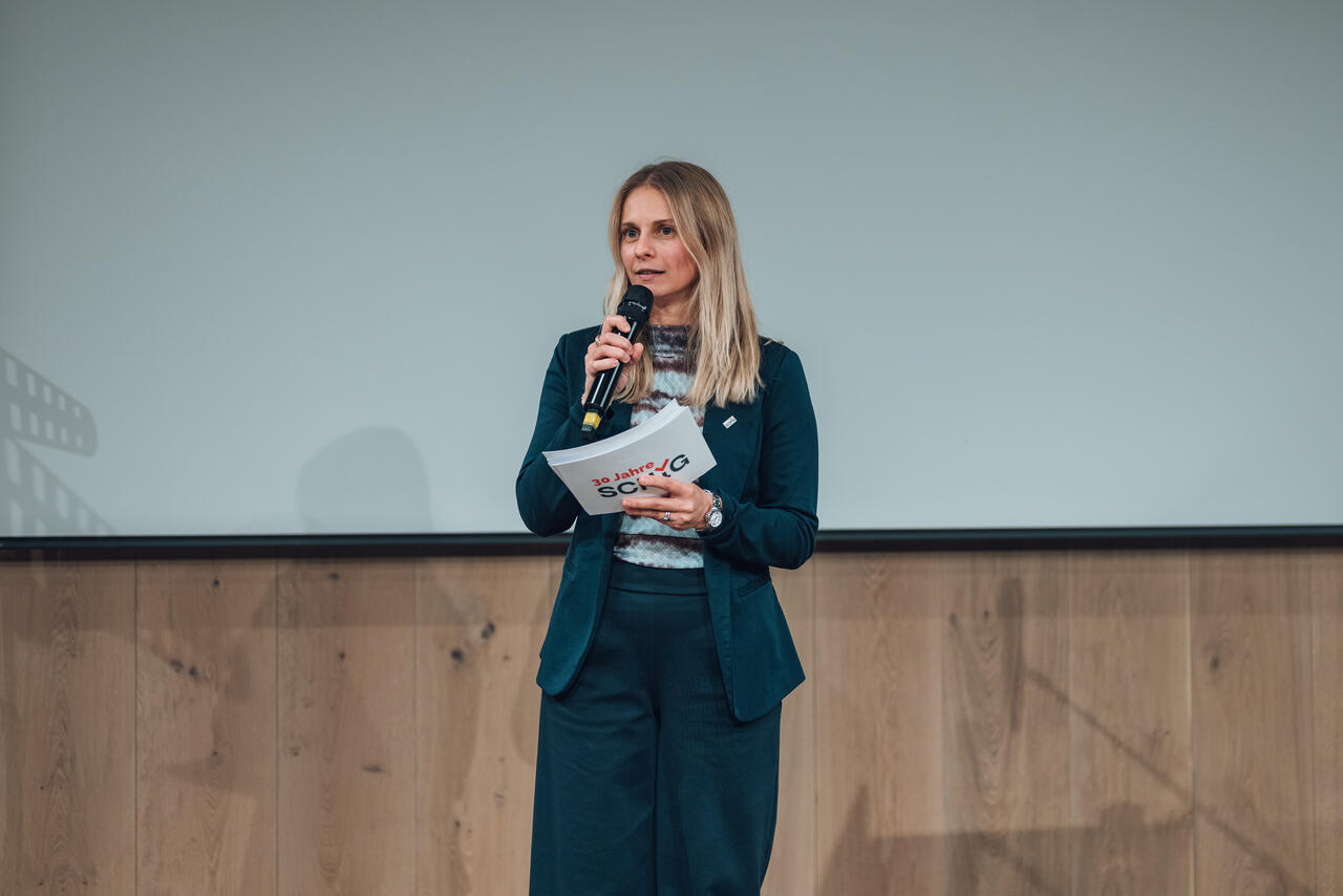 Tamara Riedl-Joven moderiert mit einem Mikrophon in der Hand.