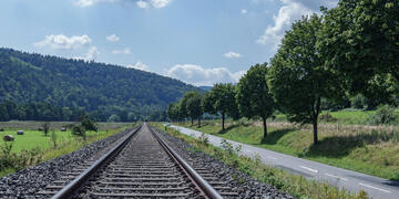 Eisenbahnschienen in grüner Landschaft neben einer Straße.