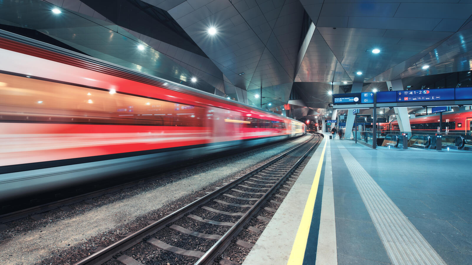 Ein roter Zug fährt durch einen Bahnhof, man sieht ihn leicht verschwommen.