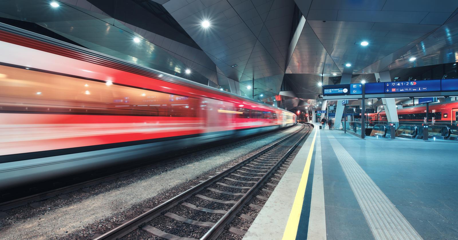 Ein roter Zug fährt durch einen Bahnhof, man sieht ihn leicht verschwommen.